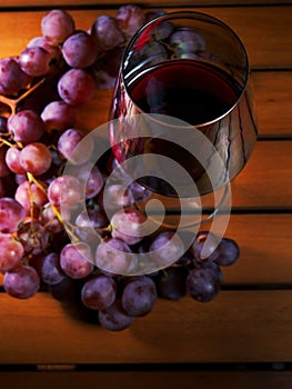 Claster of red grapes and glass of red wine on a wooden table surface. Concept wine making
