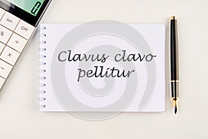 Clavus clavo pellitur. The ancient Greek expression translates as, A wedge is knocked out with a wedge. on a white notebook photo