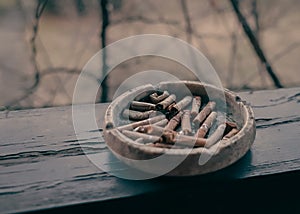 A clay ashtray with butts on a wooden terrace beam