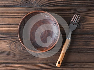 Clay bowl and fork on a brown wooden table. Flat lay.