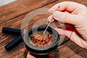 Clay bowl for hookah with coconut coals, wooden mouthpieces on a wooden background top view. Girl fills smoking tobacco.