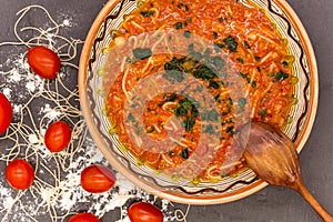 Clay bowl with traditional dish consist of tomatoes with grain noodles on slate and wooden spoon and ingredients near