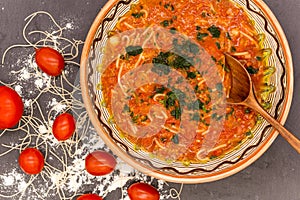 Clay bowl with traditional dish consist of tomatoes with grain noodles on slate and wooden spoon and ingredients near