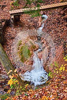 Clay carved river creek with waterfall and walking bridge in fall forest
