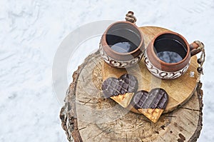 Clay cups with coffee and cookies on a wooden stump in a snowy winter forest