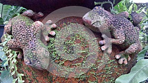 Clay Gecko sculpture with green moss on water jar in garden
