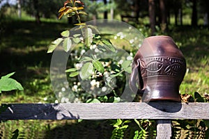 A clay jug with a pattern hangs on a wooden fence, background. Ukrainian style, art