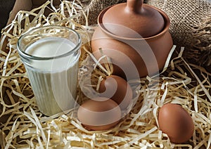 Clay jugs, eggs, glass of milk, on the straw and a burlap.