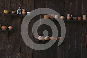 Clay jugs on a wooden shelf and a wooden dark wall