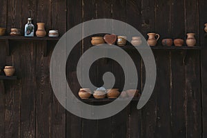 Clay jugs on a wooden shelf and a wooden dark wall