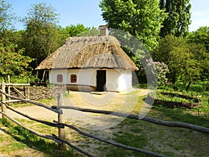 Clay old house with a thatched roof and a cozy courtyard with a drape fence and a flowerbed