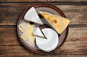 Clay plate with different cheeses on table, top view