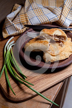 Clay plate of fried meat pies with cutlery and green onion on wooden table