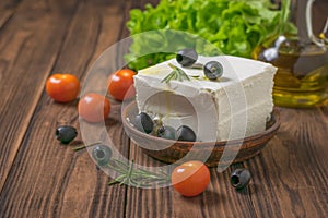 A clay plate with a piece of feta cheese , tomatoes and olives on a wooden table.