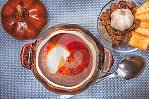 Clay pot with red soup and sour cream on a linen napkin