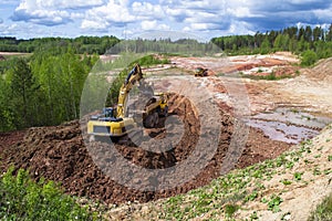 Clay quarry. The yellow excavator digs red clay with a large bucket and puts it into the truck