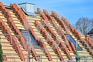 Clay roof tiles stacked on the roof of a residential house in preparation for roofing on a construction site, blue sky