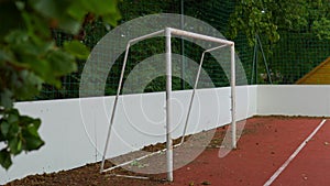 clay soccer field with white gates, green trees background