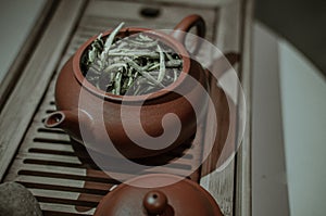 Clay tea pot with portion of white tea on a wooden table close-up
