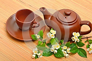 Clay teapot, teacup, saucer and jasmine flower twig on wood