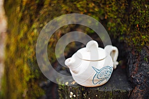 Clay white teapot with blue pattern in the forest on the stump. Handwork