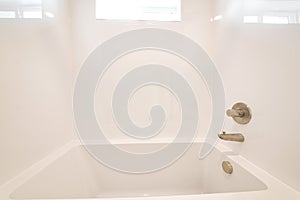 Clean bathroom with sparkling built in bathtub and shiny white tiles in the wall