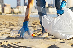 Clean beach from plastic. Hand picking up plastic bottle trash from the beach and putting into plastic bag for recycle