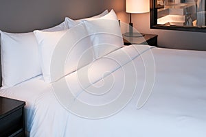 Clean Bedding sheets and pillow on natural wall room background. White bedding and pillow in hotel room. White pillows on bed.