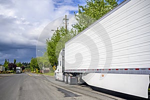 Clean big rig semi truck with high cab and refrigerated semi trailer with aerodynamic skirt standing on the street road at