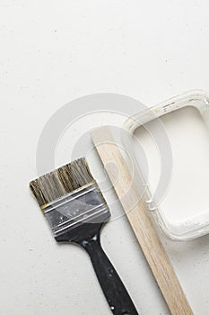 Clean black brush with piece of wood and square jar of white paint on a white table