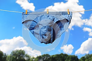 Clean blue men\'s briefs hanging on rope to dry outdoors on sunny summer day. Clothesline with washed underwear