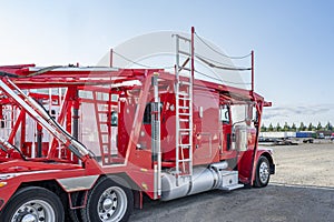 Clean bright big rigs car hauler semi trucks with hydraulic semi trailers standing in row on the industrial parking lot waiting