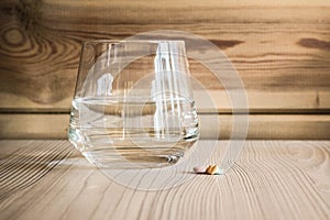 Clean clear glass with fresh water and handful of tablets medicine on wooden table and background.