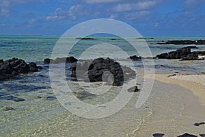 The clean clear transparent sea water off Ile aux Cerfs Mauritius with emerged black rocks and visible sandy beach