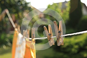 Clean clothes drying outdoors during sunny day, focus on laundry line with wooden clothespins