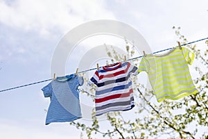 Clean clothes on rope outdoors on laundry day. Colorful t-shirts hanging on a laundry line against blue sky