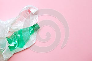Clean crumpled green plastic water bottle and white plastic bag ready for recycling isolated on pink background, top view