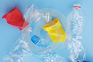 Clean crumpled plastic water bottles and colorful red and yellow disposable coffee cups ready for recycling isolated on blue backg