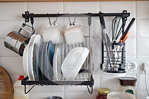 Clean dishes drying on metal dish rack on light background. Kitchen utensils and dishware. Kitchen interior background.