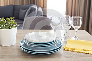 Clean dishes on the table. Stacked clean blue and white plates, glasses and yellow napkins on wooden table in the kitchen.