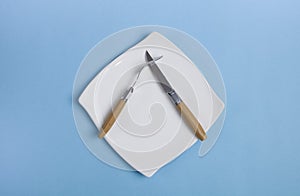 Clean empty white plate with knife and fork, on an isolated blue background