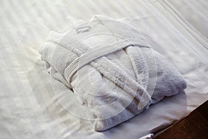 Clean folded bathrobe on white bed.