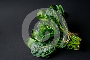 Clean food concept. Bunch of leaves of fresh organic spinach greens on a black background. Healthy detox spring-summer diet. Vegan