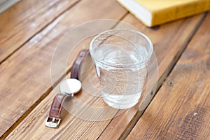 Clean glass of water on a wooden table while reading work books a clock to remind you to regularly take water a healthy lifestyle
