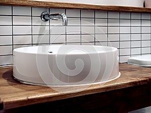 Clean modern loft style bathroom interior with wall-mount stainless steel faucet and white round shape sink basin.