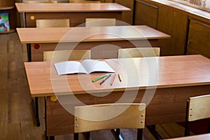 Clean notebook and colored pencils on the desk in empty classroom. Concept of school education