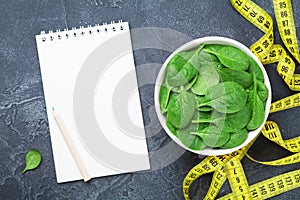 Clean notebook, green spinach leaves and tape measure top view. Diet and healthy food concept.