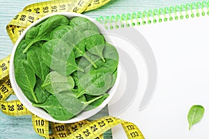 Clean notebook, green spinach leaves and tape measure on wooden table from above. Diet and healthy food concept.