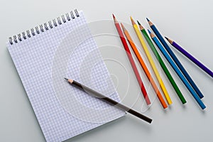 Clean notepad in a cage with a pencil lying on it and rainbow color pencils on a white background top view copy space