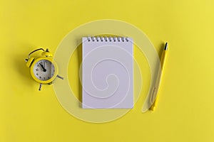 Clean Notepad, clock and pen on a yellow background, spiral notebook on the table. Business, training, education. Monochrome